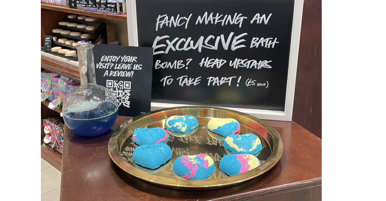 Lush invites shoppers to create some of their own bath bombs like the ones on display in front of the sign. 

