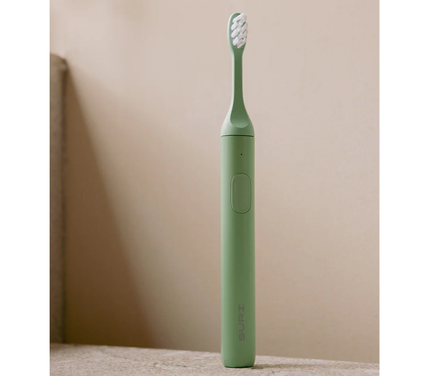 A green electric toothbrush, standing on a brown counter in front of a brown-beige wall