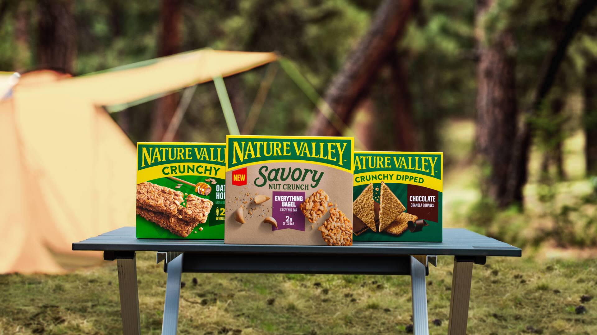 Nature Valley campaign image showing a lineup of their product boxes on a table in front of a camping tent 