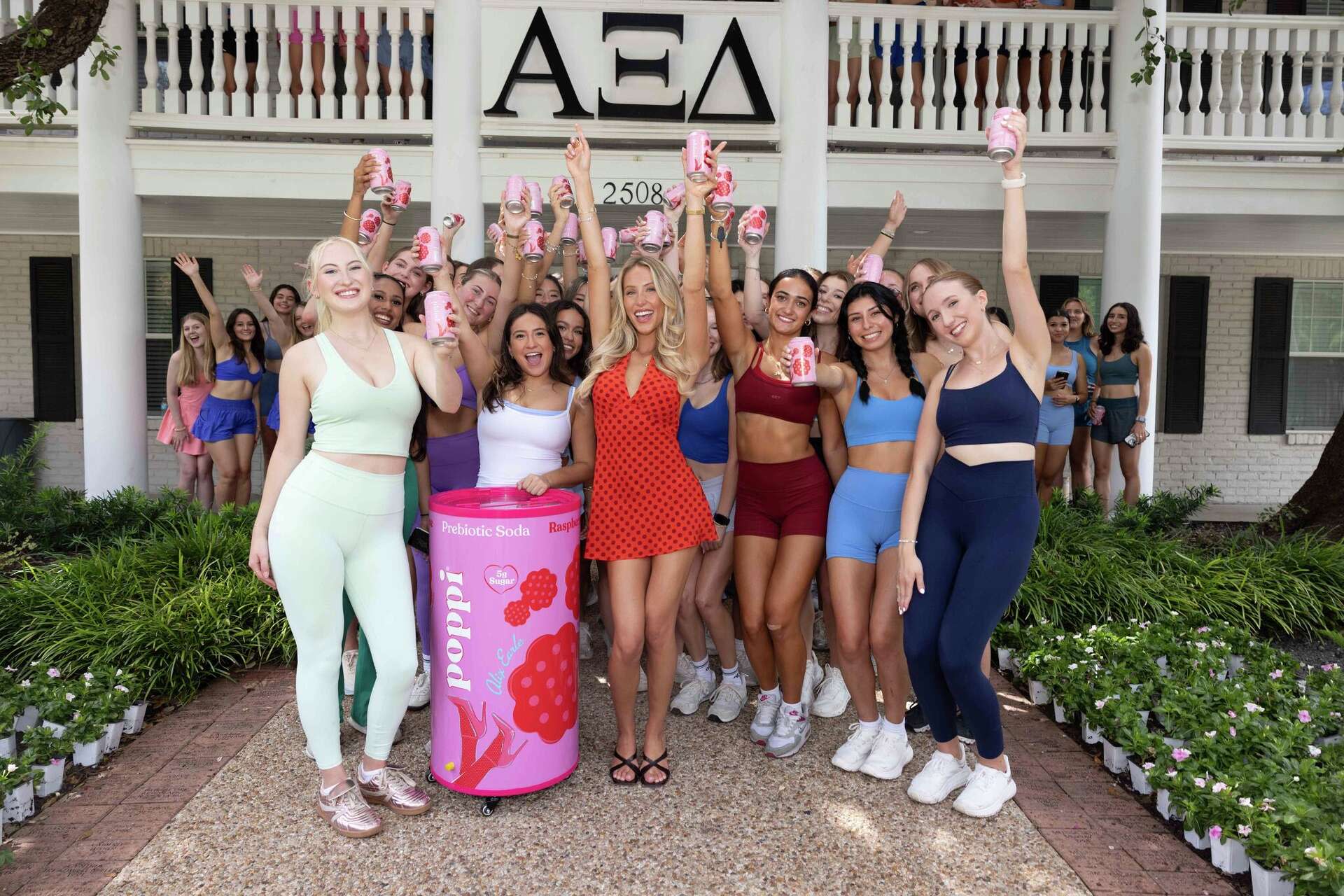 Poppi and Alix Earle influencer poses for a photo in front of a sorority house holding Poppi cans