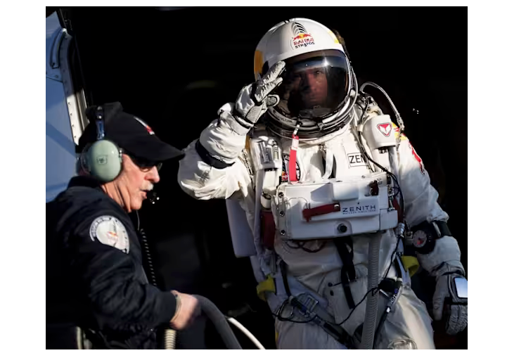 an image of a man in a space suit, saluting with a gloved hand, and in the foreground a white man with a mustache and glasses, with earphones and a microphone and black ball cap. The background is black, making you think of outer space. 