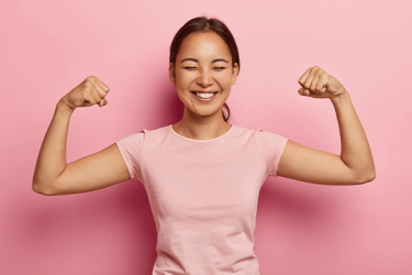 Uma mulher jovem e sorridente a mostrar a sua força, levantando os braços e punhos fechados