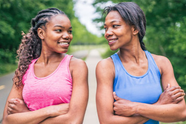 Duas mulheres - uma jovem e outra de meia-idade - a olhar para si e a sorrir amavelmente. No fundo encontra-se uma estrada e árvores verdes