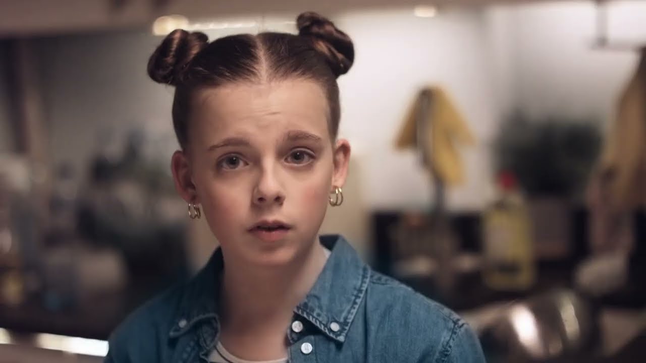 Little girl with two buns looking towards the camera with a surprised look on her face.