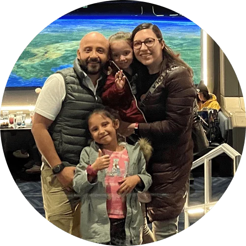 An adult woman, adult man, and two young girls pose together in the Space 220 Restaurant at the Walt Disney World Resort. The restaurant windows simulate a panoramic view of Earth from outer space.