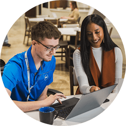 Two P&G employees sitting at a desk smiling and looking at a laptop in one of P&G's meeting spaces.
