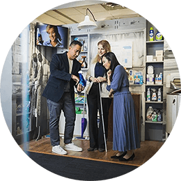 A Hispanic male, white female and Asian female stand in a mid-century model laundry room. They are looking at a blue dish detergent bottle that the male employee is holding.