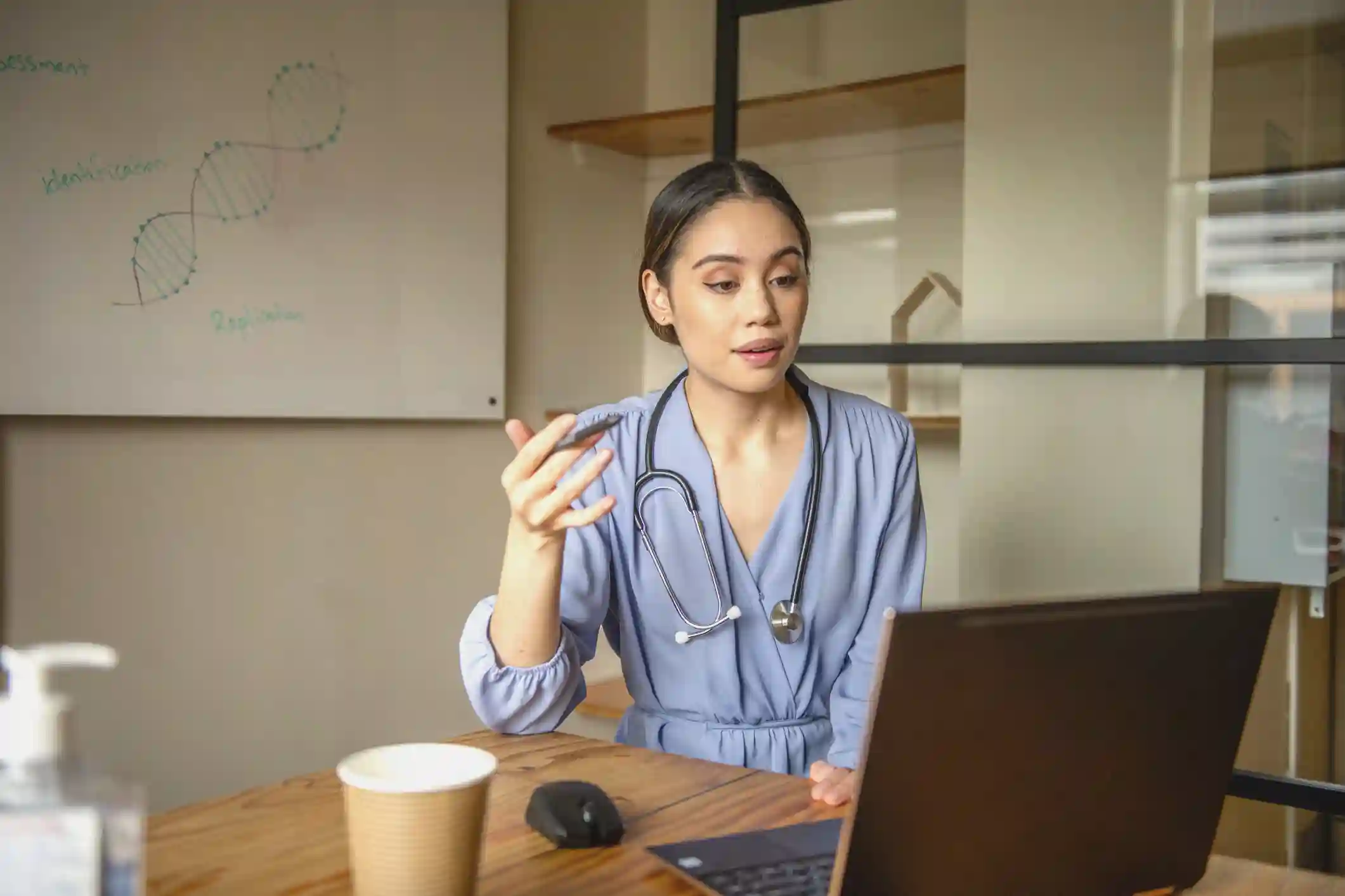 A doctor sits at a table speaking to a patient over a video conference