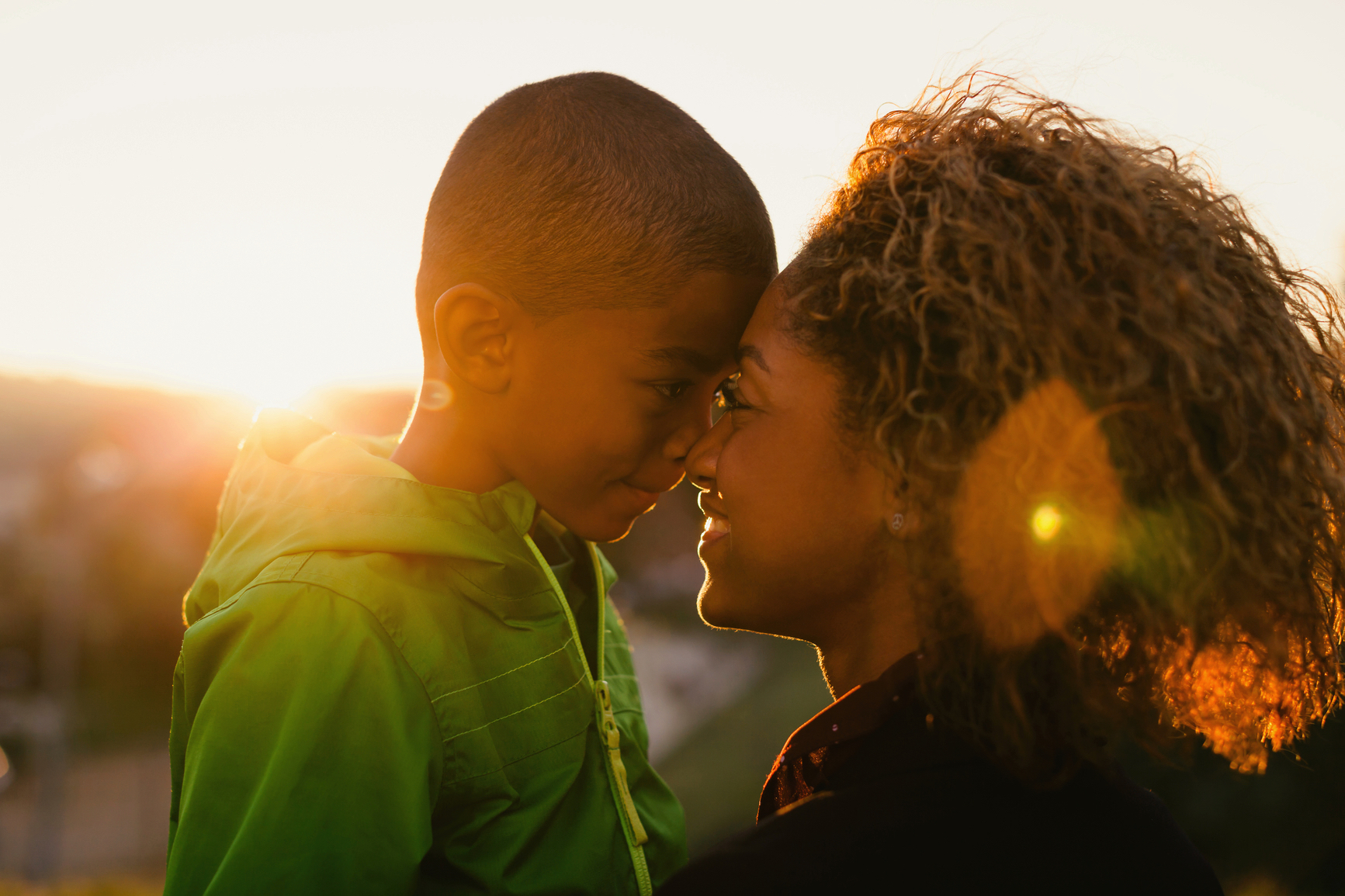 A woman and child embracing and touching foreheads while the sun sets in the background