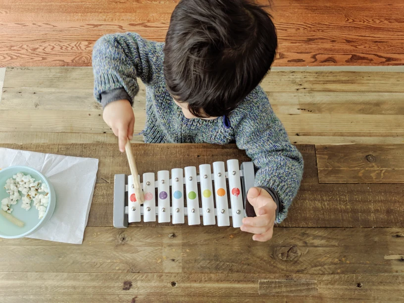 Child playing with a small xylophone and eating popcorn