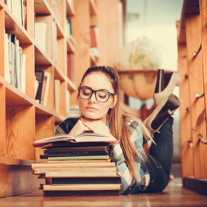 Studierende liegt auf dem Boden und liest Bücher für's Studium
