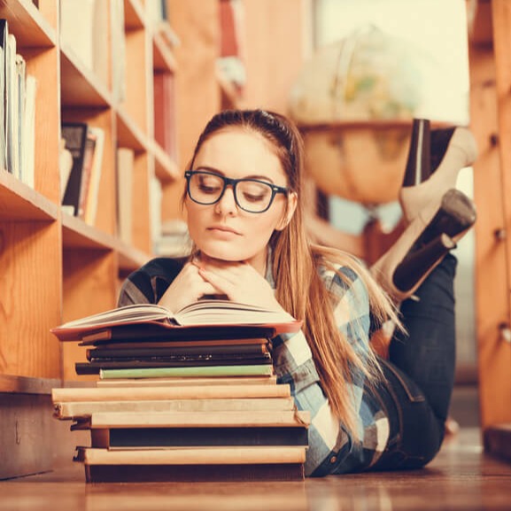 Studierende liegt auf dem Boden mit einem Stapel Studienliteratur