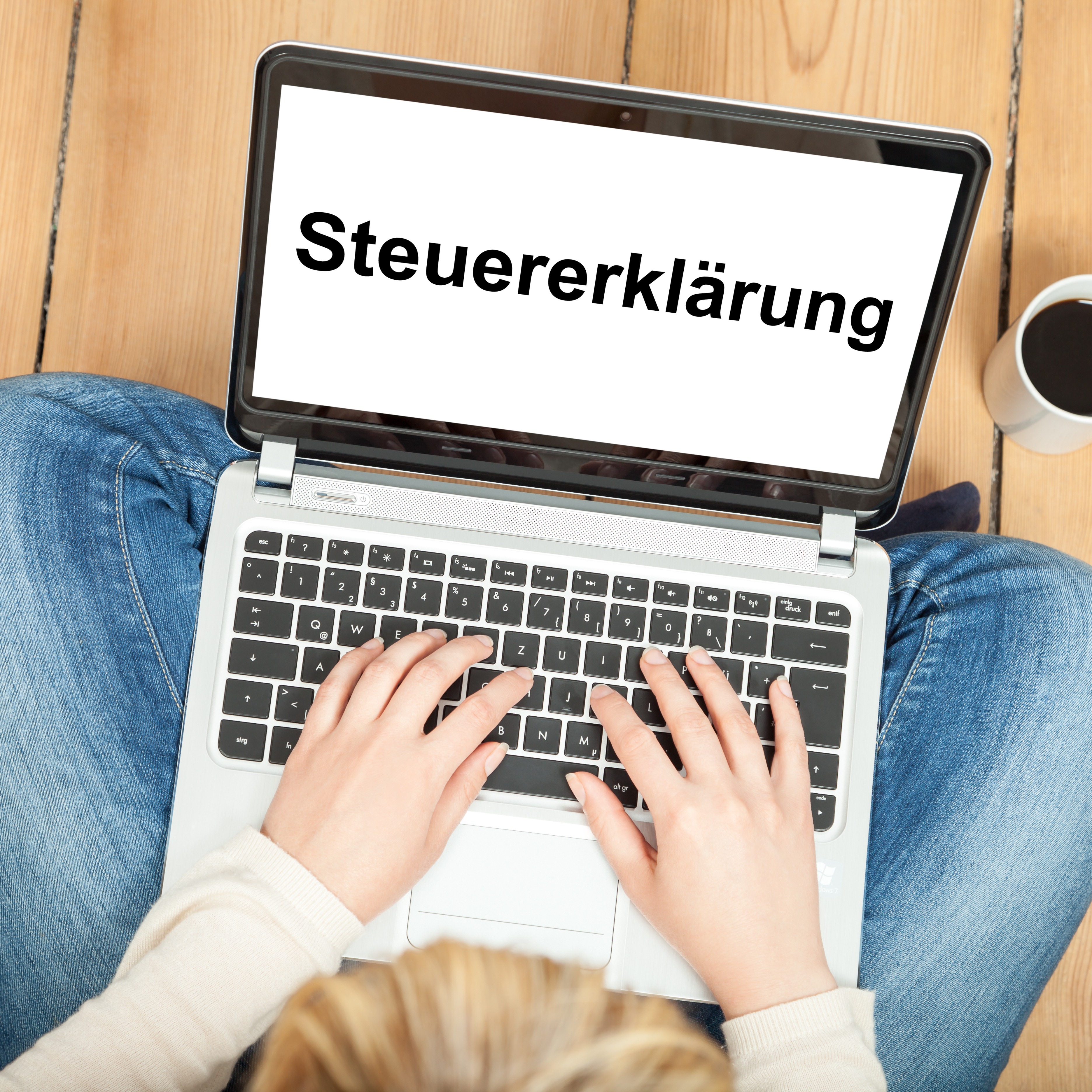 Frau sitzt auf dem Boden am Laptop und macht Steuererklärung