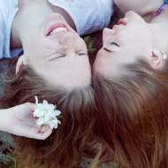 2 Freundinnen liegen lachend zusammen auf der Wiese