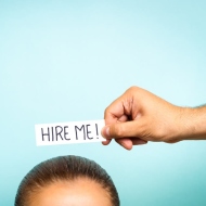 Über den Kopf einer Person wird ein Schild mit der Aufschrift: "Hire Me" gehalten