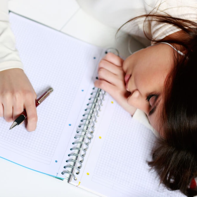 Studierende schläft mit dem Kopf auf dem Schreibtisch