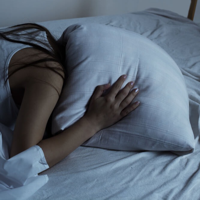 Studierende begräbt schalflos ihren Kopf unter dem Kissen