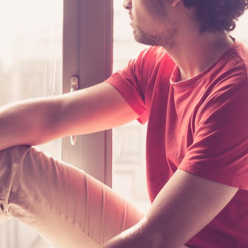 Junger Studierender sitzt am Fenster und schaut nachdenklich nach draußen
