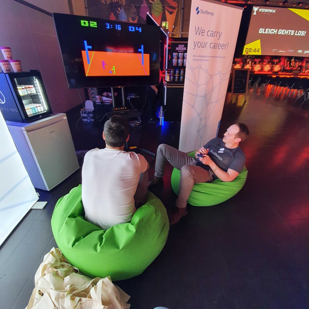 Zwei Messebesucher spielen am Studitemps Stand mit der Retro Konsole