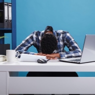 Junger Mann sitzt ermüdet und überfordert am Arbeitsplatz