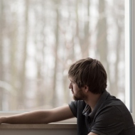 Junger Mann schaut nachdenklich aus dem Fenster