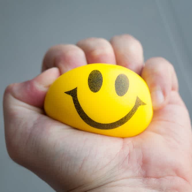Person hält gelben Anti-Stress-Ball mit glücklichem Smiley in der Hand