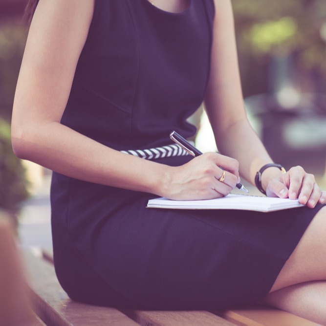 Studierende sitzt draußen und notiert sich etwas für ihren Nebenjob