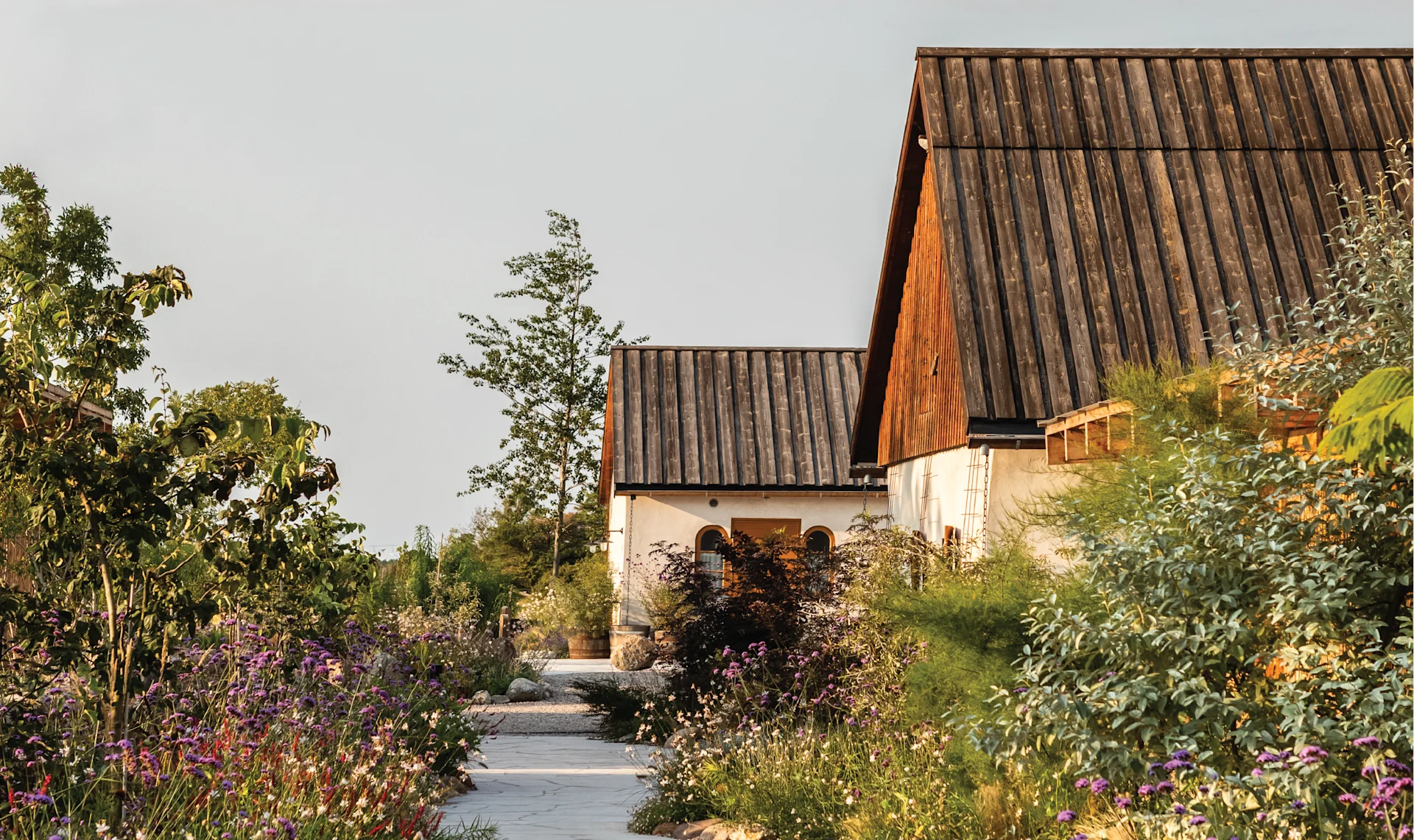 Left: Flower-filled garden with stone paths outside a white countryside building. Right: Two sheep standing in a grassy paddock near a wooden fence.