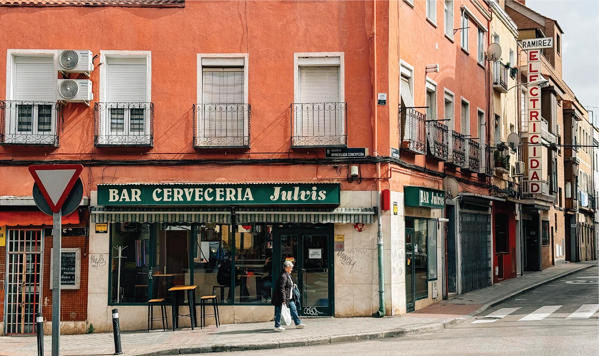Corner bar and café in Carabanchel with a green “Bar Cervecería Julián” sign on a terracotta-colored building along a quiet Madrid street.
