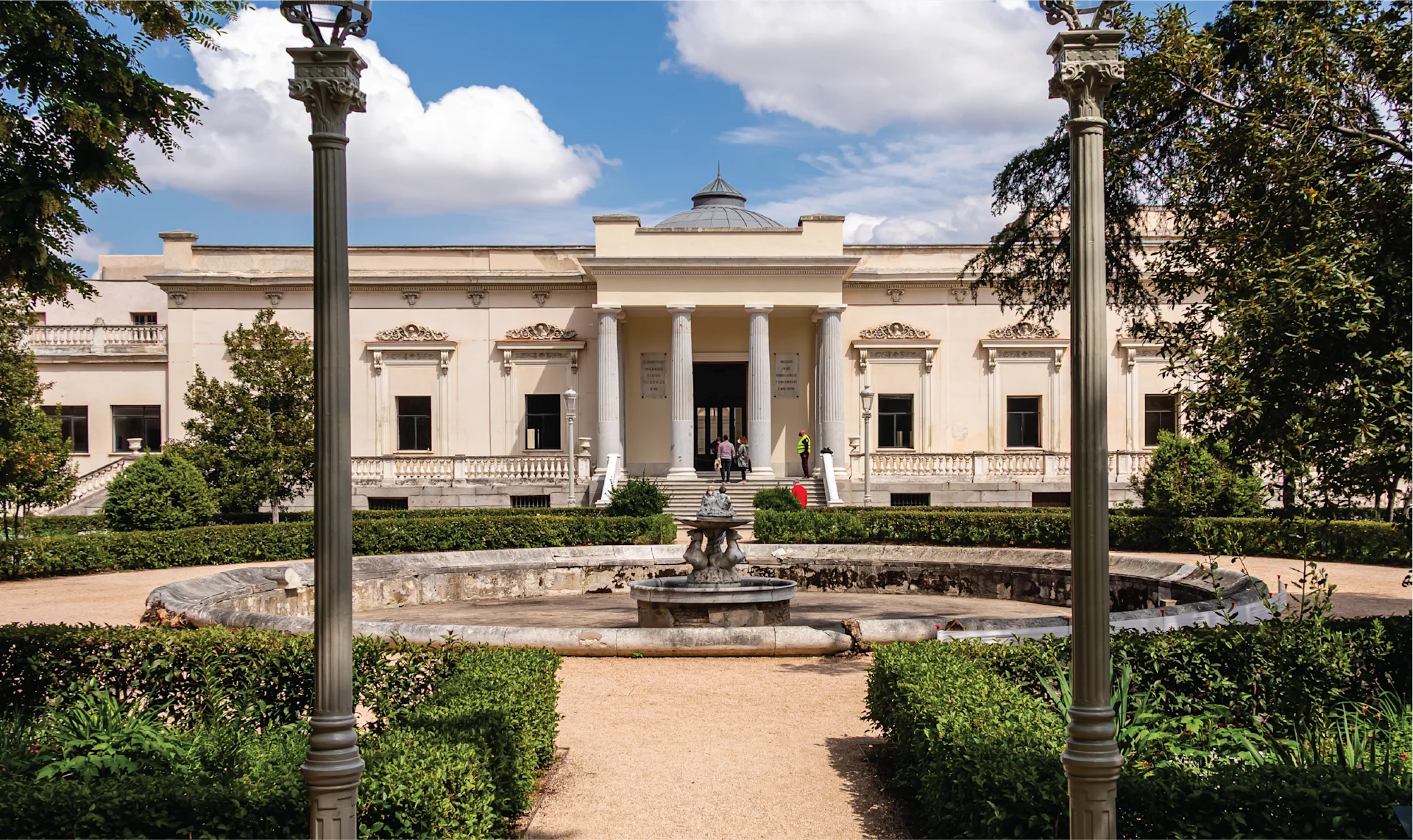 Neoclassical façade of Quinta de Vista Alegre palace in Madrid, framed by garden paths, trimmed hedges, and a central fountain.