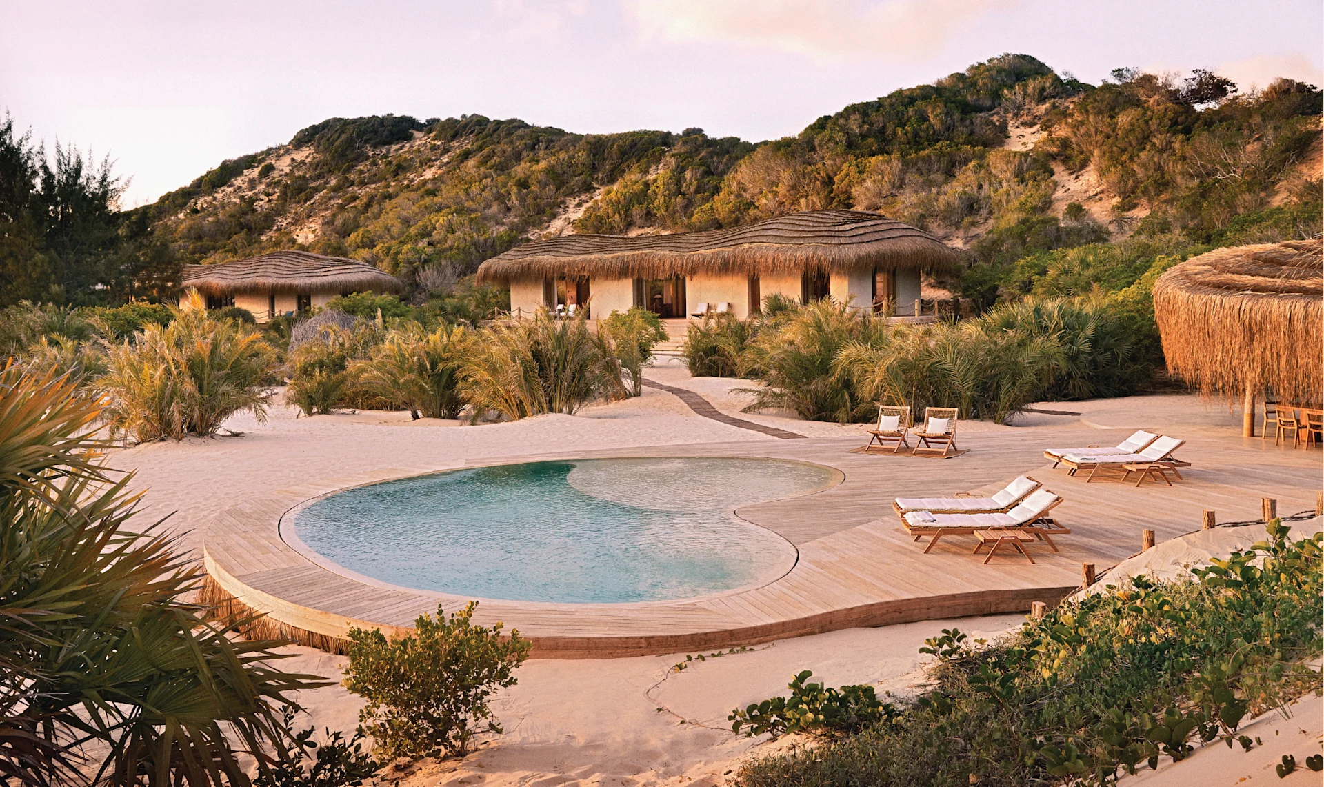 Golden-hour or sunset view over Kisawa Sanctuary, showing villas silhouetted against warm light with the ocean horizon in the background.