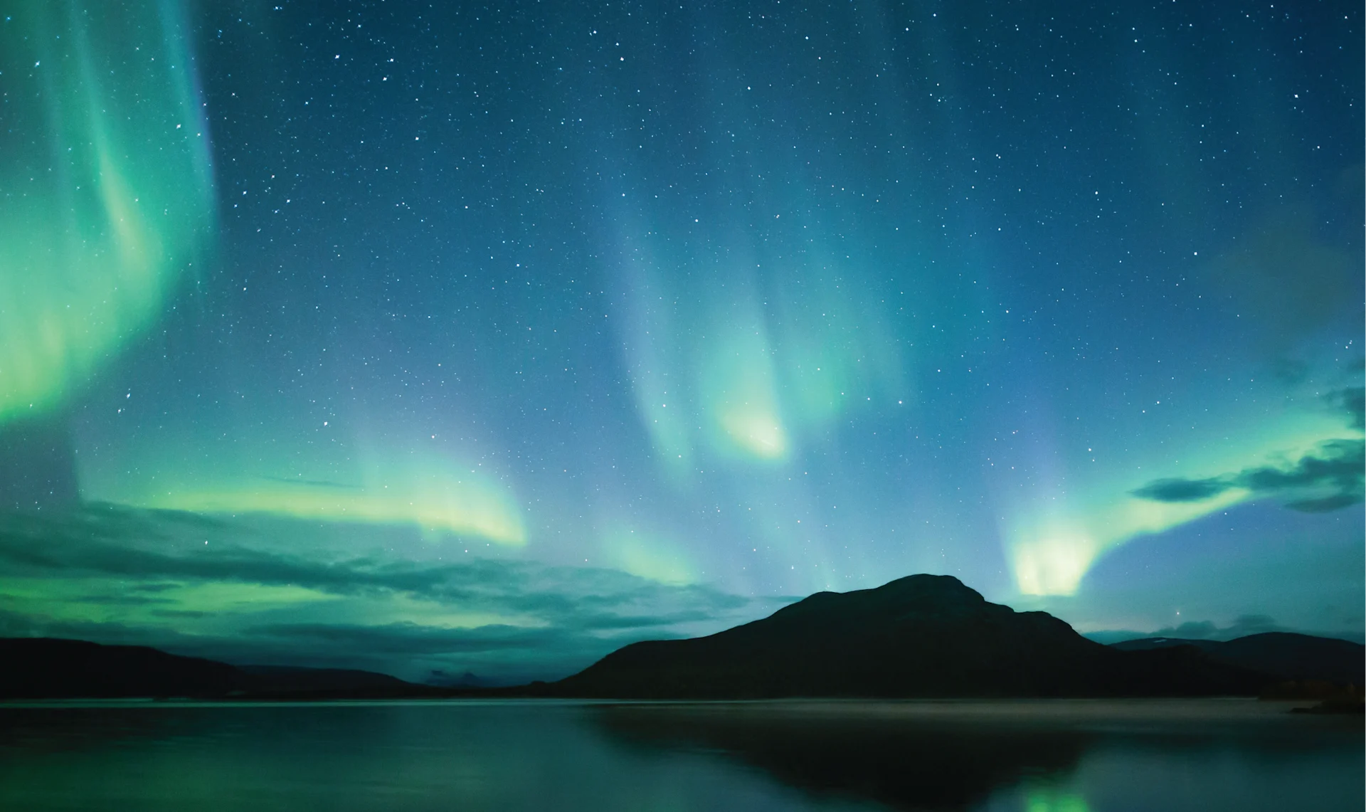 The Northern Lights seen over a snowy landscape in Finland, glowing in green and violet waves across a clear night sky