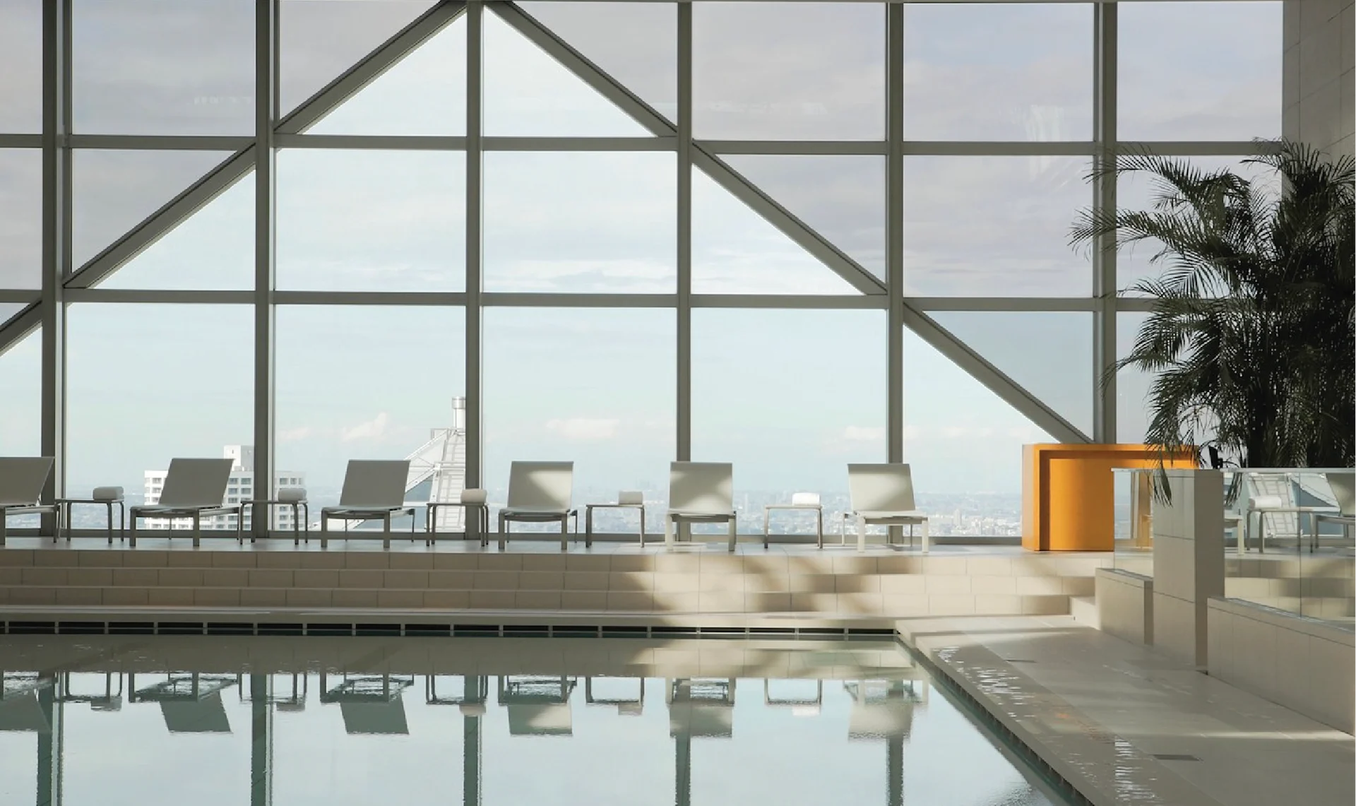 Indoor swimming pool at Park Hyatt Tokyo with floor-to-ceiling windows, lounge chairs overlooking the city, and soft natural light reflecting on the water.