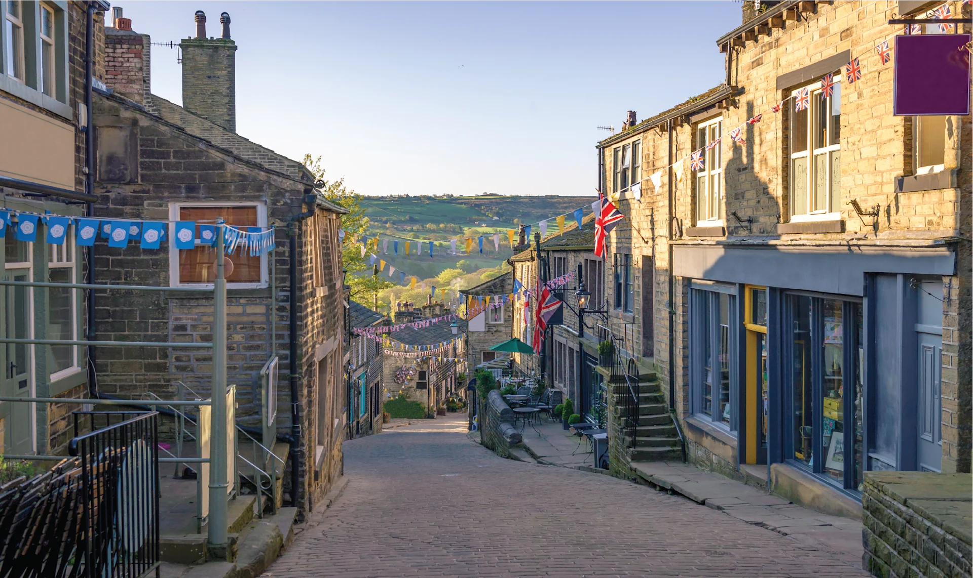 Stone houses lining the sloping main street of Haworth village, leading toward the moorland horizon under a muted northern sky.