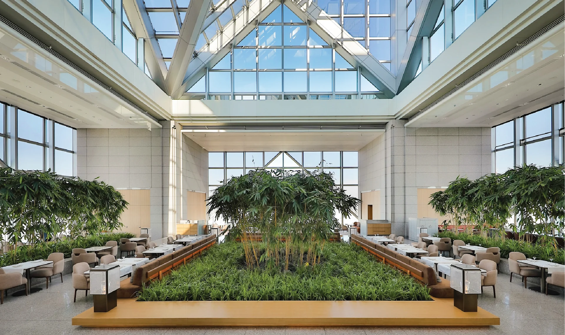 Bright Peak Lounge at Park Hyatt Tokyo featuring a glass ceiling, indoor greenery, and minimalist lounge seating arranged around a central garden.