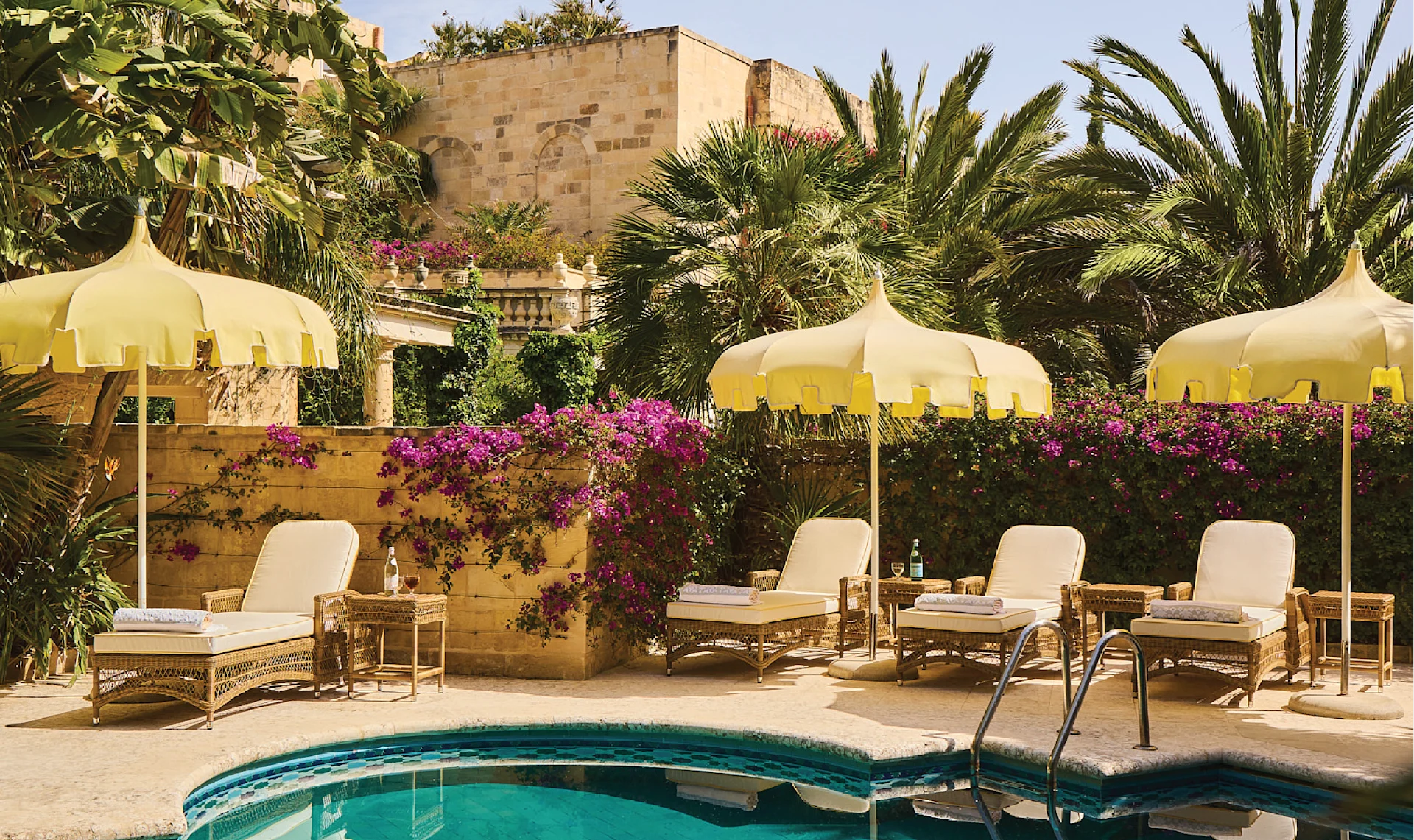 Swimming pool at Casa Bonavita surrounded by tropical gardens, flowering bougainvillea, vintage-style yellow parasols, and luxurious sun loungers.