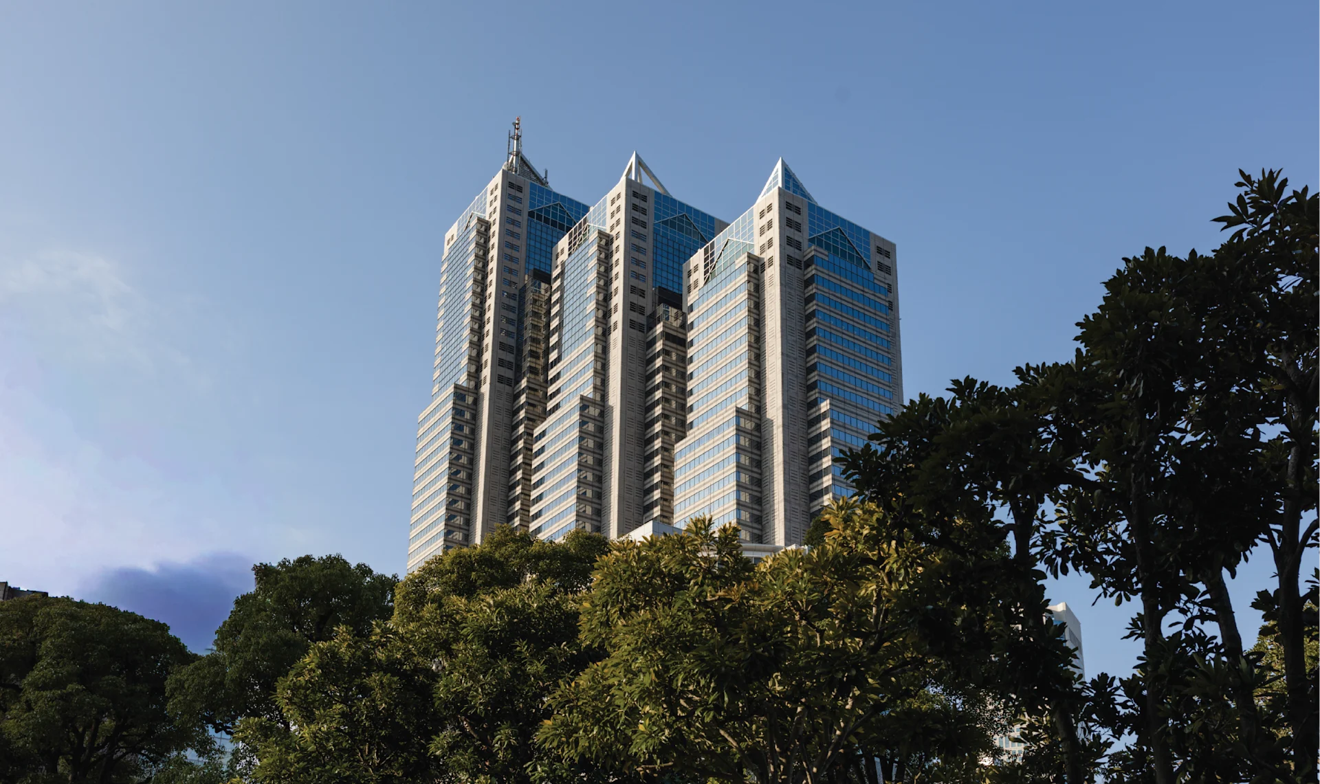 Exterior view of the high-rise towers of Park Hyatt Tokyo rising above lush green trees against a clear blue sky.