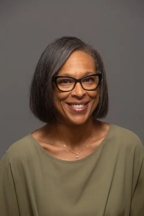 Woman of color in olive green shirt with dark-framed eye glasses and short black hair