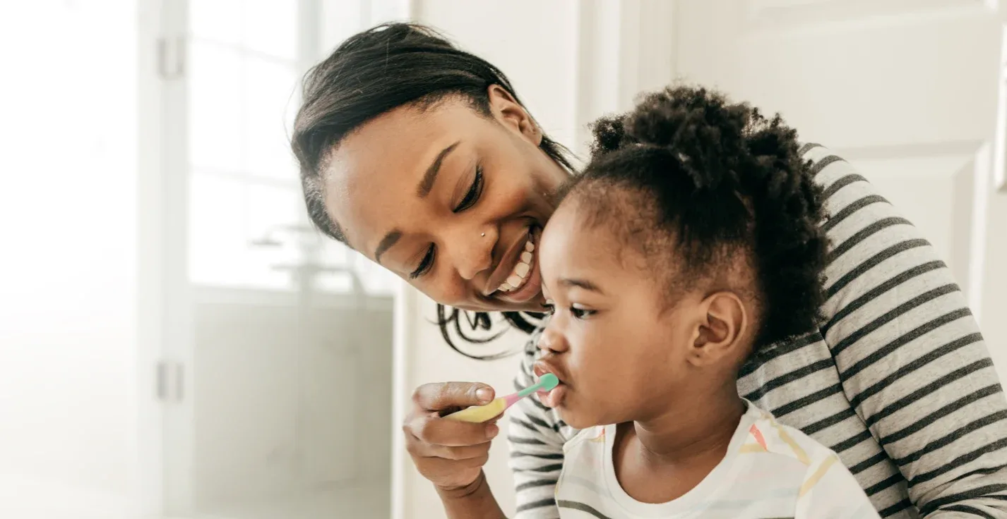 A lady brushing kid's teeth 