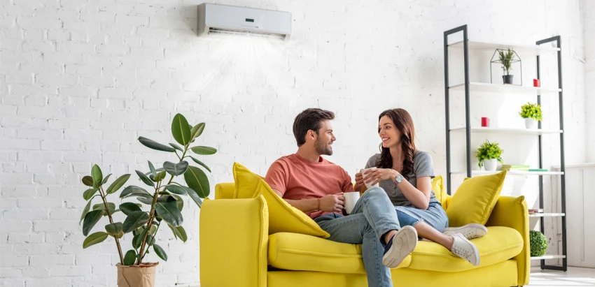 casal sentado em sofá amarelo numa sala com ar condicionado ligado