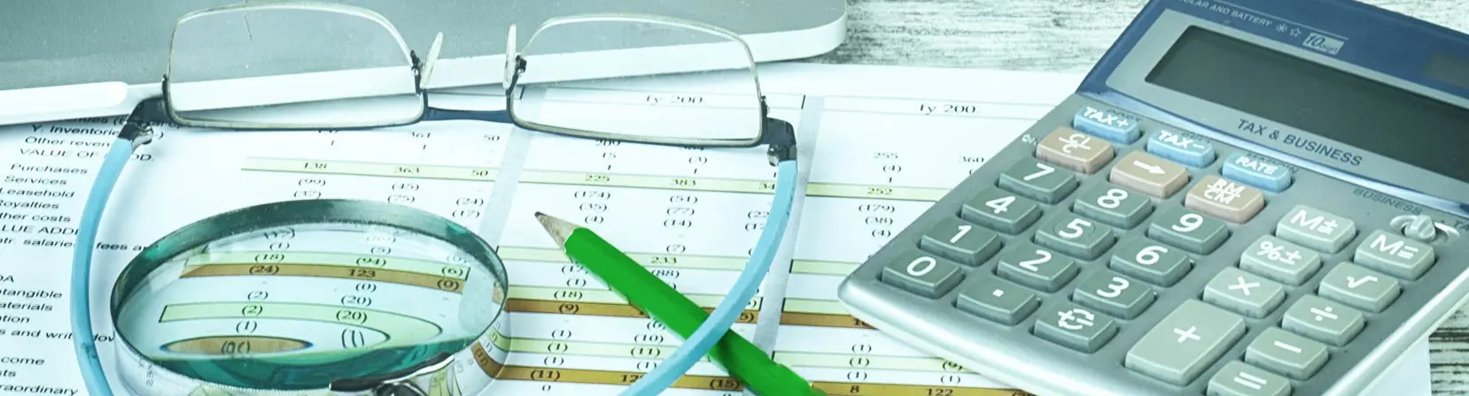 máquina de calcular, óculos, lupa e um lápis em cima de uma mesa