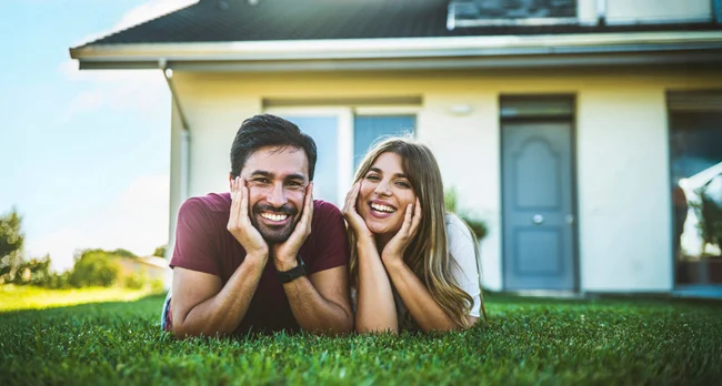 Casal feliz, deitado na relva, depois de renovar a casa com o apoio do assistente de renovação da DECO PROteste.
