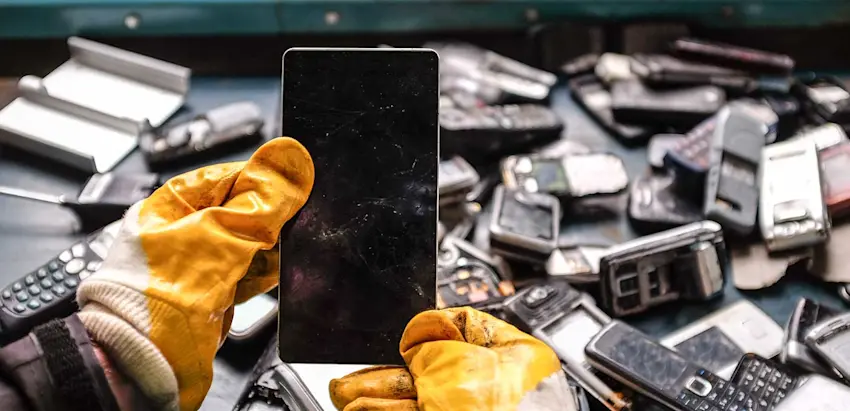 Mãos com luvas a segurar um telemóvel no meio de resíduos eletrónicos