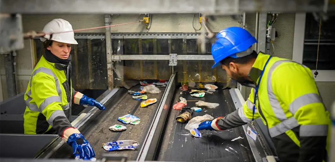 Funcionários a separar itens numa correia transportadora numa instalação de gestão de resíduos