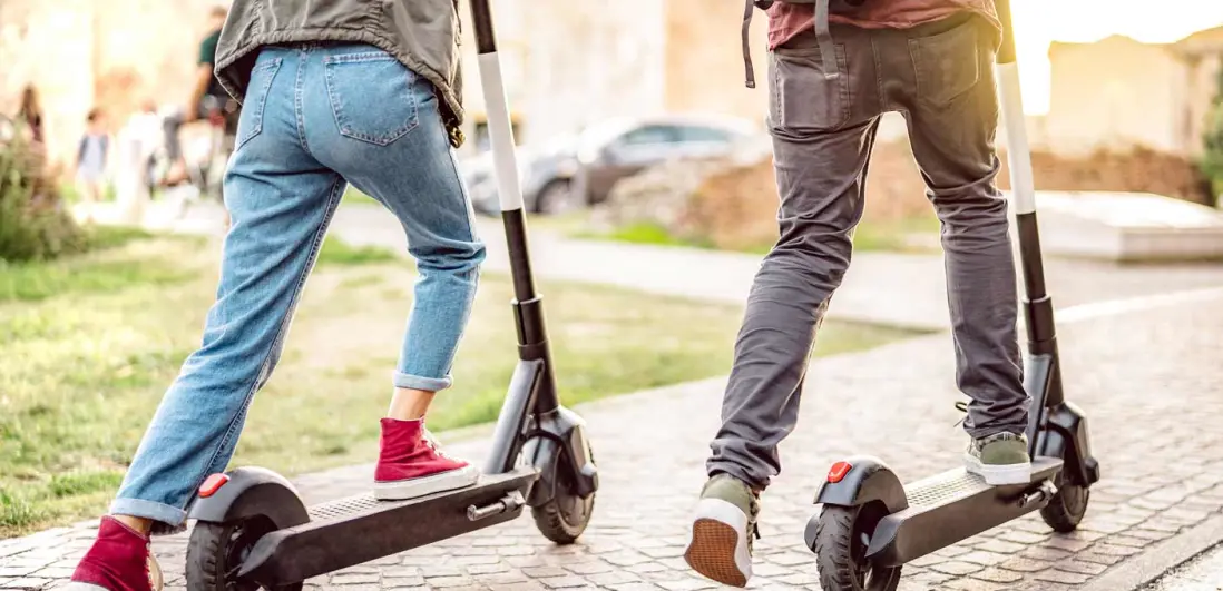 duas pessoas a andar de trotinete na rua