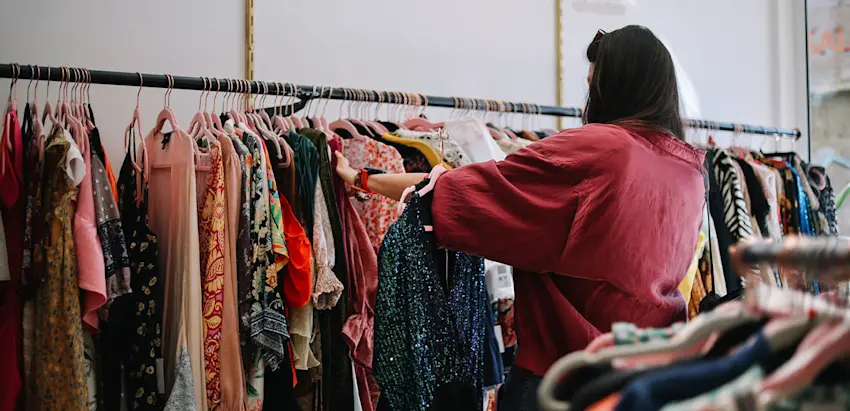 Pessoa a observar roupa colorida pendurada num varão numa loja, segurando várias peças no braço
