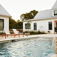 Modern white farmhouse-style home with swimming pool, lounge chairs, and water feature in the backyard.