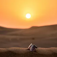 Person walking alone in the desert dunes at sunset with the sun low in the sky.