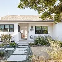 Modern white house with landscaped front yard, stone walkway, and black-framed windows.