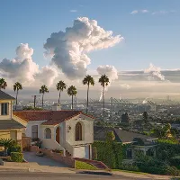Scenic coastal neighborhood with palm trees, houses, and clouds rising over the ocean horizon.